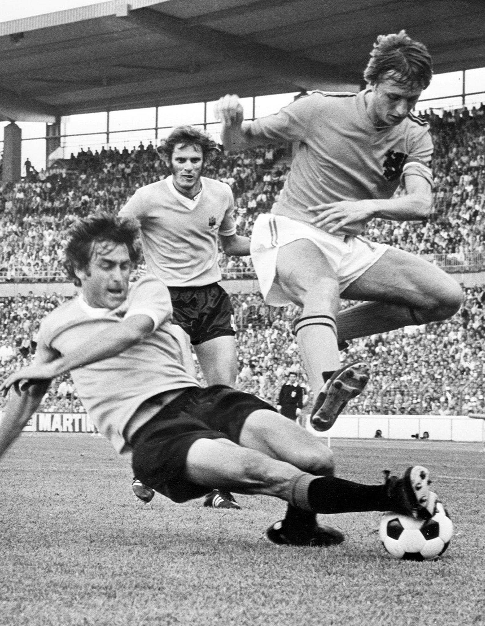 Aquí el holandés salta a la barrida del defensor uruguayo Ricardo Pavoni. Observa Baudilio Jauregui. Partido del 15 de junio 1974 en Hannover, durante la Copa del Mundo de Alemania. Holanda se impuso 2-0. Foto AFP.