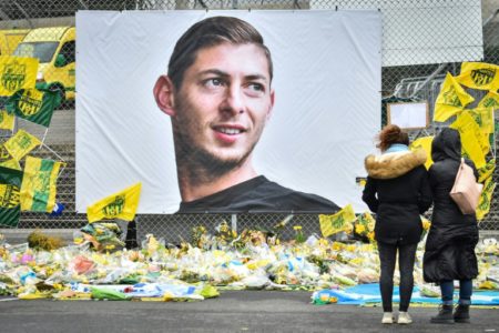 Dos mujeres contemplan los ramos de flores y banderines dejados ante un retrato de Emiliano Sala