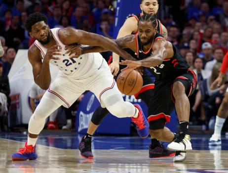 Kawhi Leonard, de los Toronto Raptors, alcanza el balón mientras retiene a Joel Embiid de los 76ers de Filadelfia