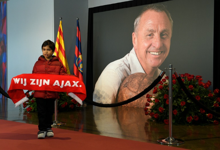 Un niño simpatizante del club holandés Ajax posa junto a una gigantografía del fallecido astro del fútbol Johan Cruyff en una zona dedicada a su memoria en el estadio Camp Nou de Barcelona el 26 de marzo de 2016 / AFP / LLUIS GENE